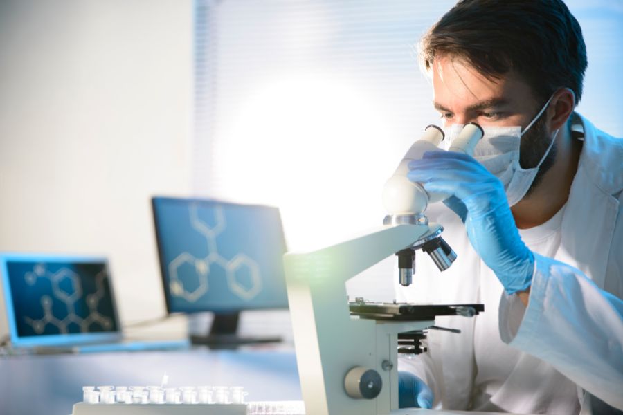 Un chercheur en blouse blanche et gants bleus utilise un microscope en laboratoire pour la recherche scientifique moderne.
